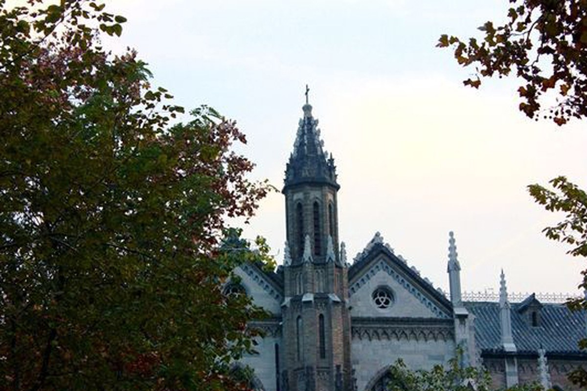 A slender historic tower rising above trees against a pale sky.